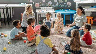 Two teachers sitting on a rug with seven children