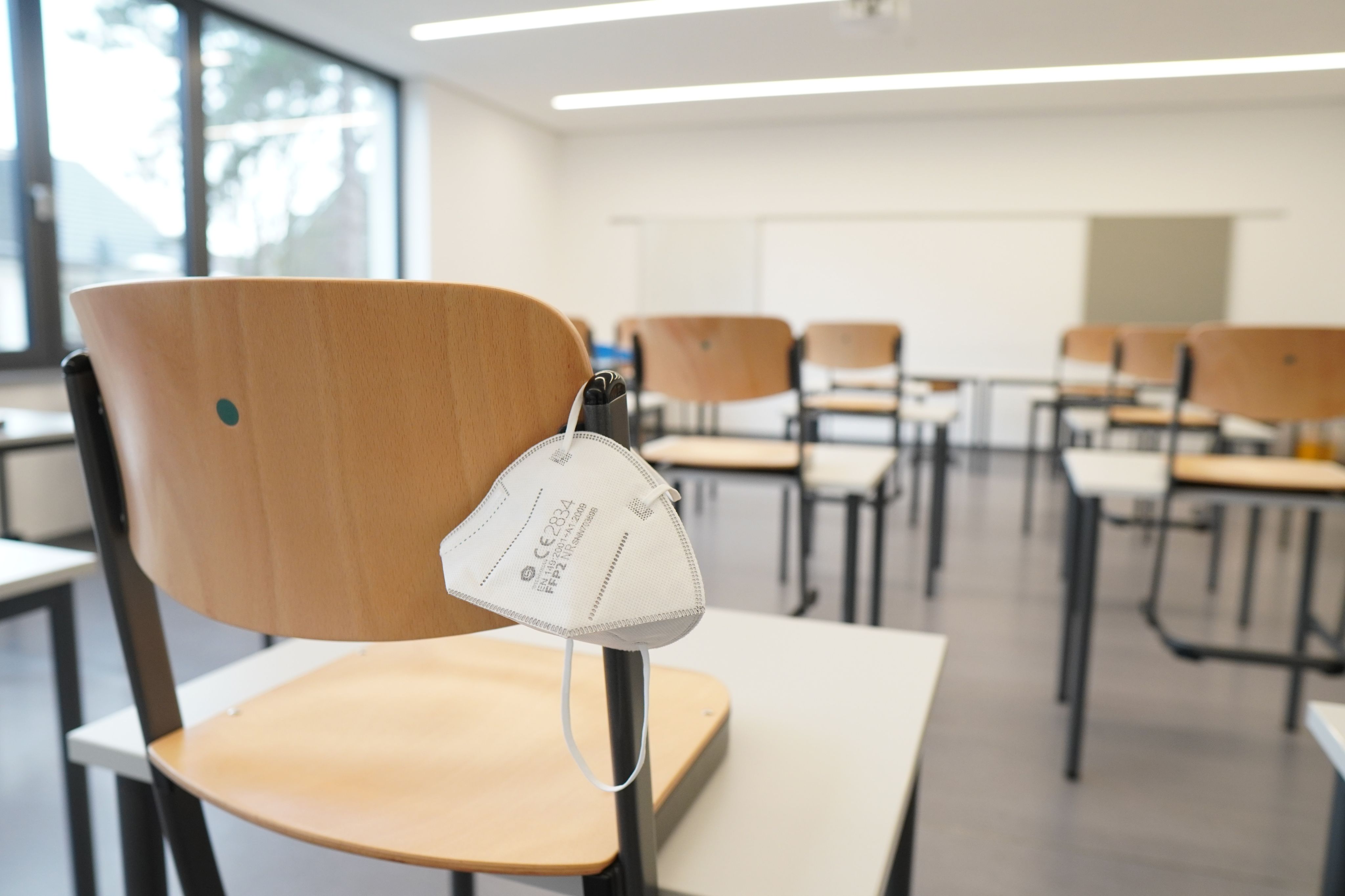 empty desks in a classroom with a medical mask hanging on one desk