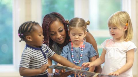 Photo of a Black teacher and three toddlers